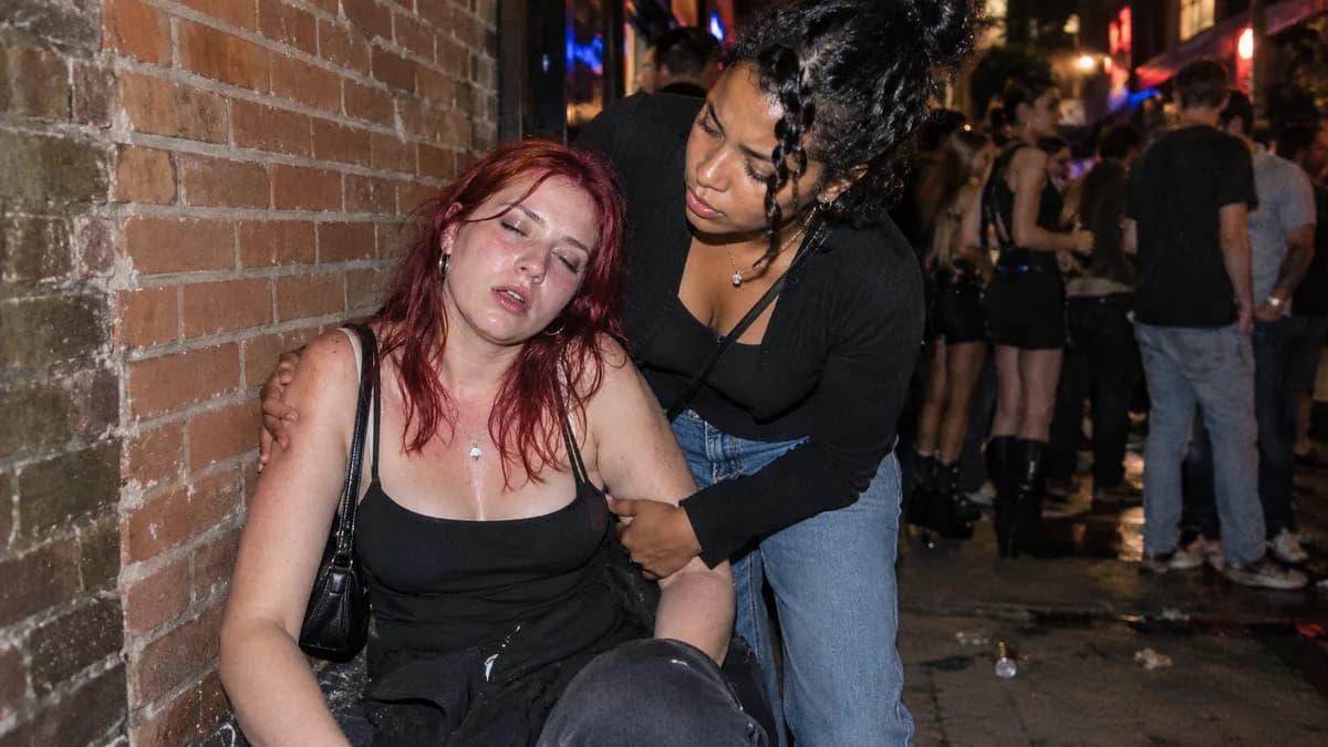 Une femme en détresse est soutenue par une amie dans une rue bondée, illustrant les dangers de l'alcoolisation excessive chez les jeunes.